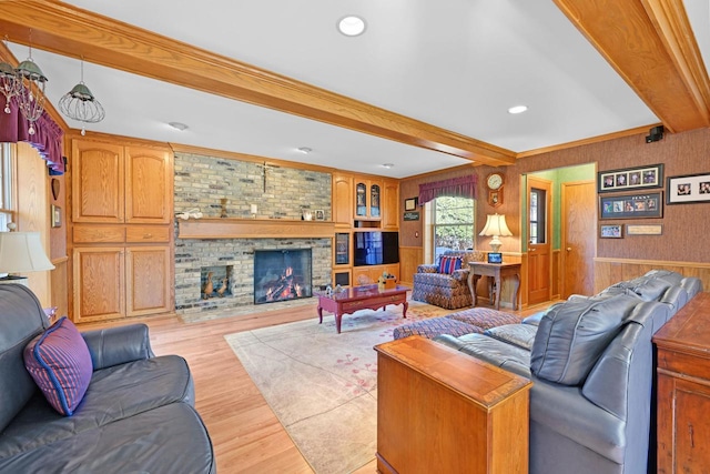 living room featuring a wainscoted wall, beam ceiling, light wood-style flooring, wood walls, and a brick fireplace