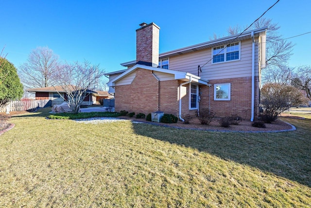 rear view of property with fence, a lawn, brick siding, and a chimney