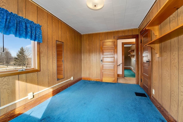 carpeted empty room featuring wooden walls and visible vents