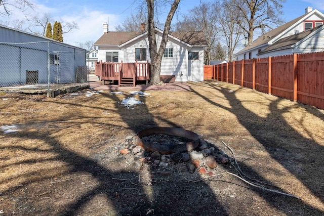 back of property featuring a chimney, a fire pit, a wooden deck, and a fenced backyard