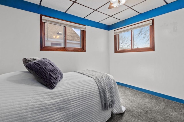 carpeted bedroom featuring baseboards, a drop ceiling, and ceiling fan