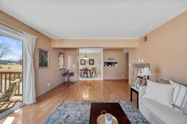 living room with visible vents, baseboards, light wood finished floors, and a chandelier