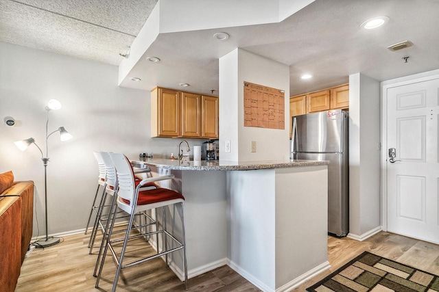 kitchen with a kitchen breakfast bar, light wood finished floors, and freestanding refrigerator