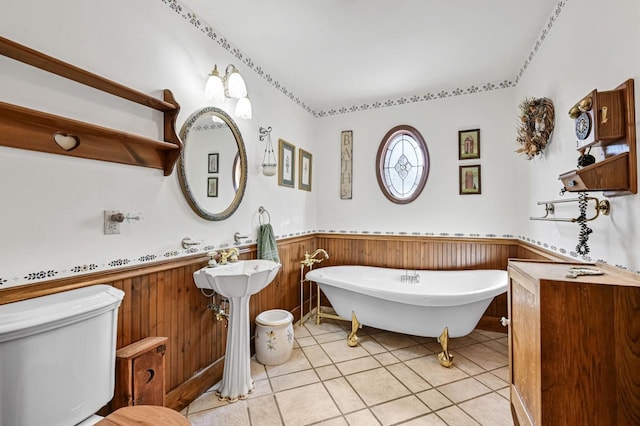 full bath with a soaking tub, tile patterned flooring, wood walls, wainscoting, and toilet