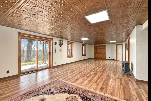 unfurnished living room featuring a wood stove, wood finished floors, baseboards, and an ornate ceiling