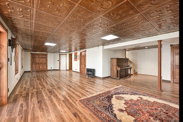 finished below grade area with an ornate ceiling, wood finished floors, brick wall, baseboards, and stairs