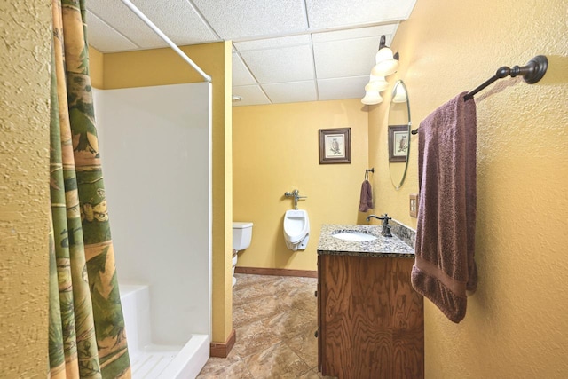 bathroom with baseboards, a drop ceiling, toilet, a stall shower, and vanity