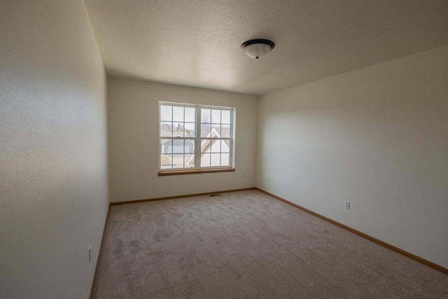 spare room with light colored carpet, baseboards, and a textured ceiling