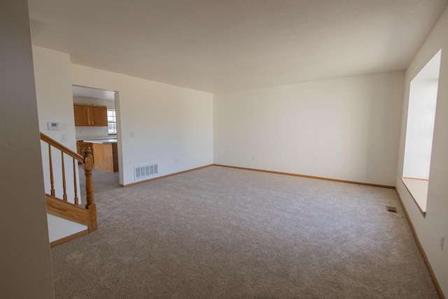 spare room featuring visible vents, light carpet, baseboards, and stairs