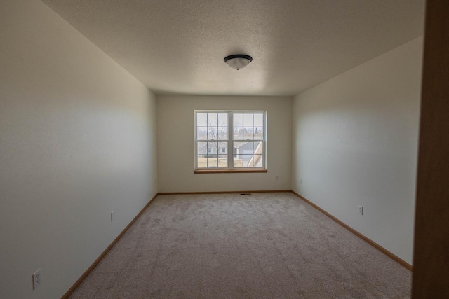 empty room with light colored carpet, baseboards, and a textured ceiling