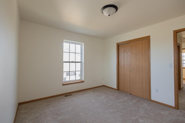 unfurnished bedroom featuring a closet, baseboards, light colored carpet, and visible vents