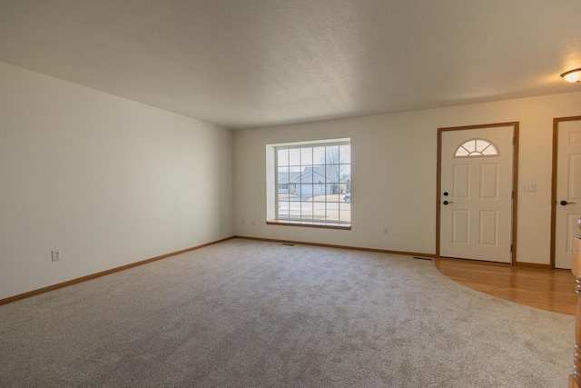 foyer entrance with light colored carpet, a textured ceiling, and baseboards