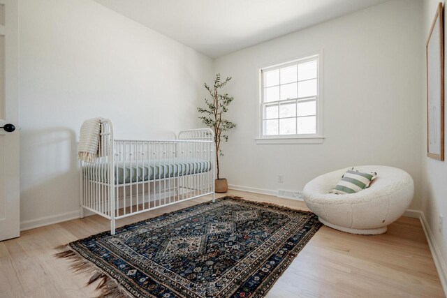 bedroom with visible vents, baseboards, a nursery area, and wood finished floors