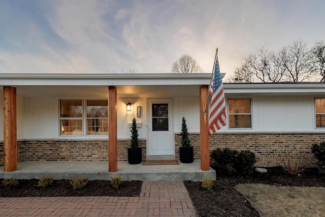 doorway to property featuring brick siding and covered porch