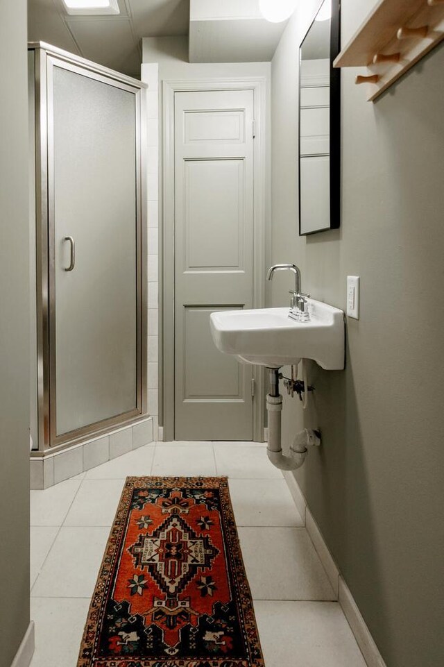 bathroom featuring tile patterned flooring, a stall shower, baseboards, and a sink