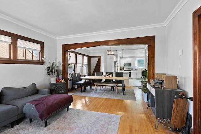 living area featuring light wood-style floors, a healthy amount of sunlight, ornamental molding, and an inviting chandelier