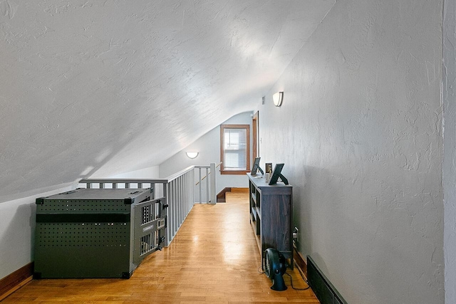 bonus room with vaulted ceiling, a textured wall, light wood-type flooring, and a textured ceiling