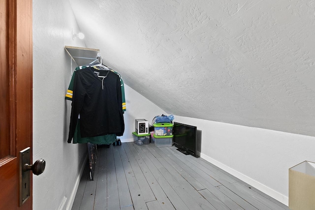 additional living space with baseboards, wood-type flooring, a textured ceiling, and vaulted ceiling