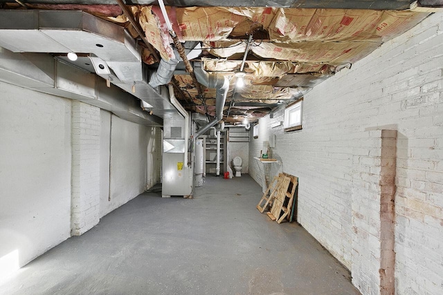 basement featuring heating unit, brick wall, and water heater