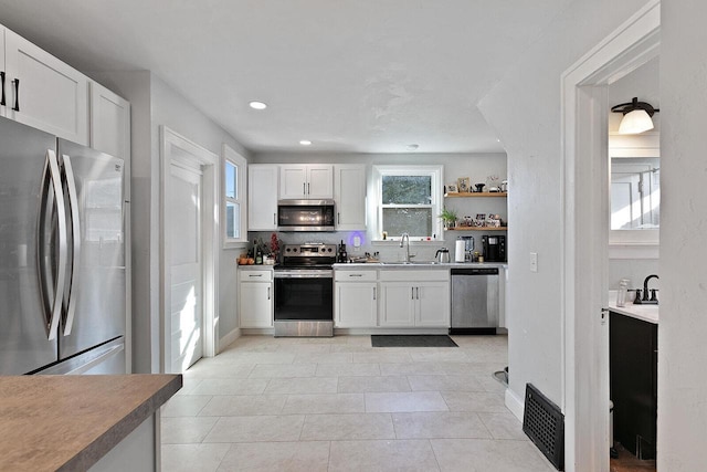 kitchen with white cabinets, light tile patterned flooring, appliances with stainless steel finishes, and a sink