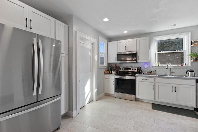 kitchen with tasteful backsplash, light tile patterned floors, appliances with stainless steel finishes, white cabinets, and a sink