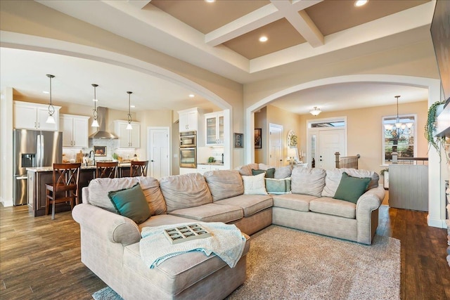 living area with arched walkways, coffered ceiling, and dark wood-type flooring