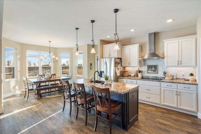 kitchen with white cabinets, wall chimney exhaust hood, dark wood-style floors, and stainless steel refrigerator with ice dispenser