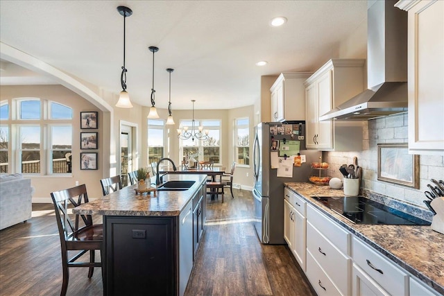 kitchen with wall chimney range hood, dark wood finished floors, a breakfast bar, black electric cooktop, and a sink