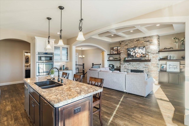 kitchen with a sink, arched walkways, appliances with stainless steel finishes, a breakfast bar area, and stacked washer / drying machine