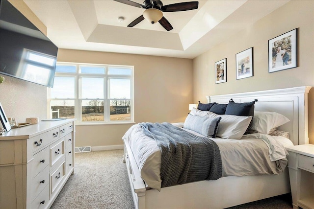 bedroom featuring visible vents, light carpet, a raised ceiling, a ceiling fan, and baseboards