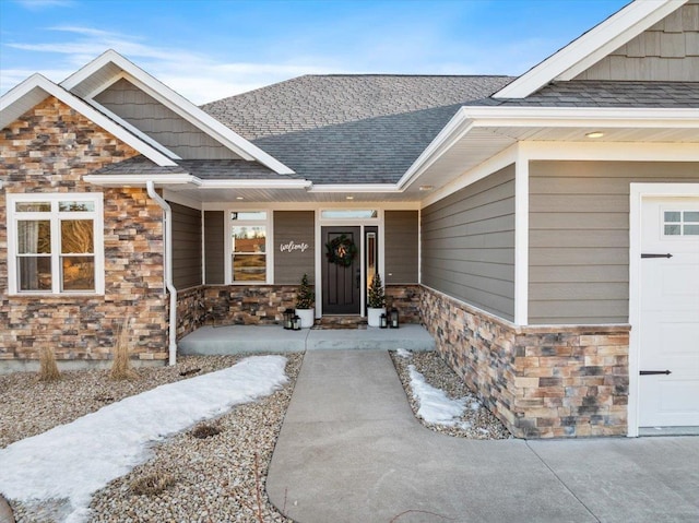 property entrance featuring stone siding, a garage, and roof with shingles