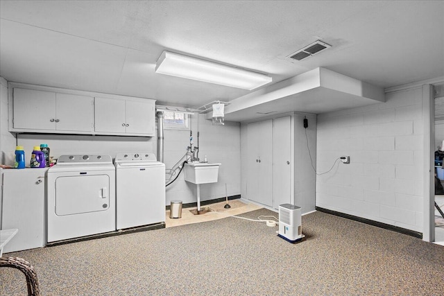 clothes washing area with visible vents, washer and dryer, cabinet space, concrete block wall, and a sink