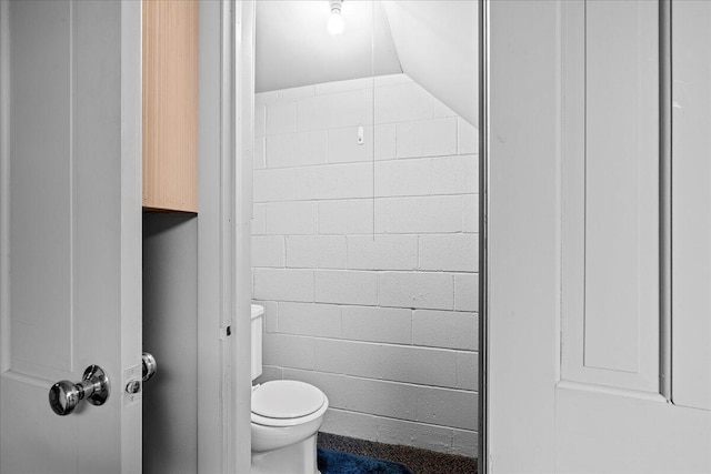 bathroom with lofted ceiling, concrete block wall, and toilet