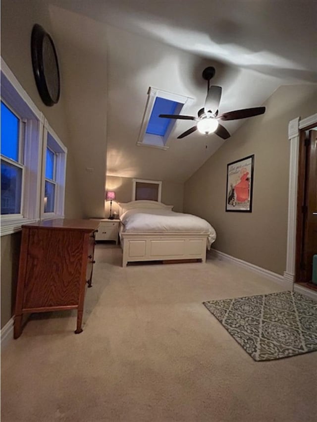 carpeted bedroom featuring vaulted ceiling with skylight, a ceiling fan, and baseboards