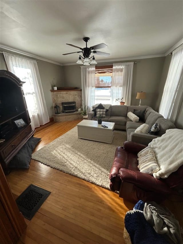 living room with visible vents, a fireplace with raised hearth, hardwood / wood-style flooring, crown molding, and ceiling fan