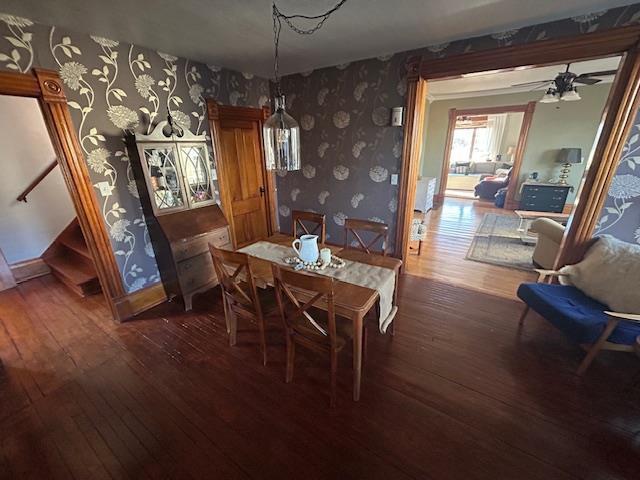 dining space featuring wallpapered walls, stairway, dark wood finished floors, and baseboards