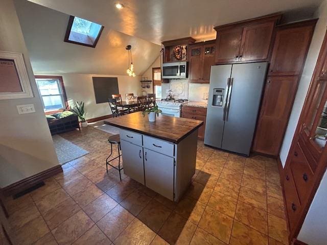 kitchen featuring a kitchen island, baseboards, lofted ceiling with skylight, appliances with stainless steel finishes, and a kitchen breakfast bar