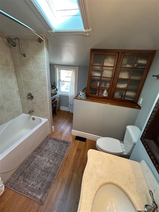 full bath featuring wood finished floors, baseboards, vaulted ceiling with skylight, shower / washtub combination, and toilet