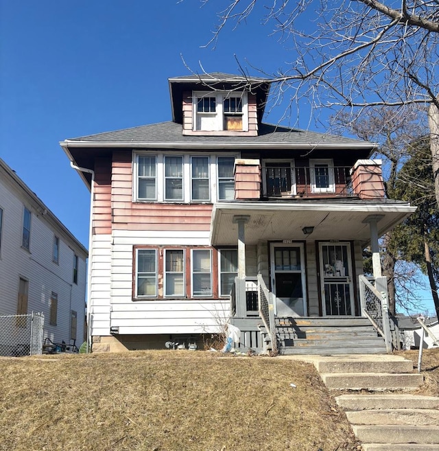 american foursquare style home with a balcony, covered porch, a front lawn, and fence