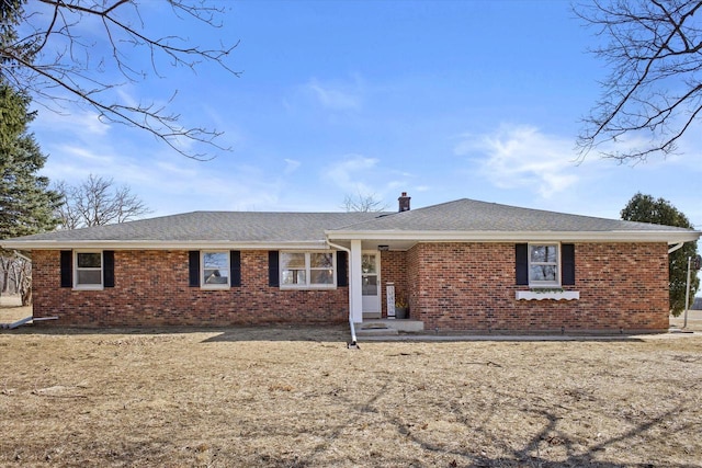 ranch-style house featuring a shingled roof, brick siding, and a chimney