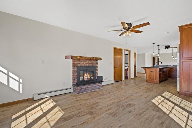 unfurnished living room with a baseboard heating unit, light wood finished floors, a baseboard radiator, a brick fireplace, and ceiling fan