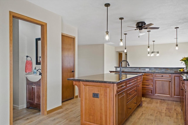 kitchen featuring brown cabinets, light wood-type flooring, a center island with sink, and a sink