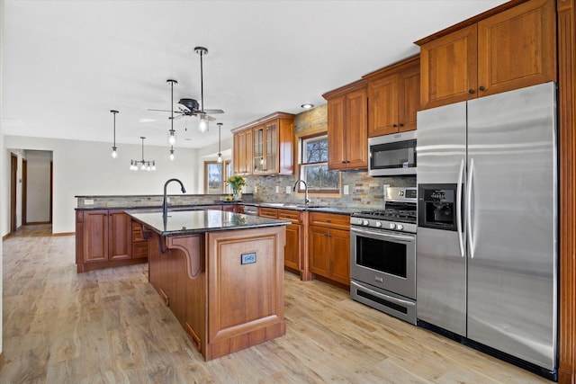 kitchen featuring brown cabinetry, light wood finished floors, a peninsula, stainless steel appliances, and decorative backsplash