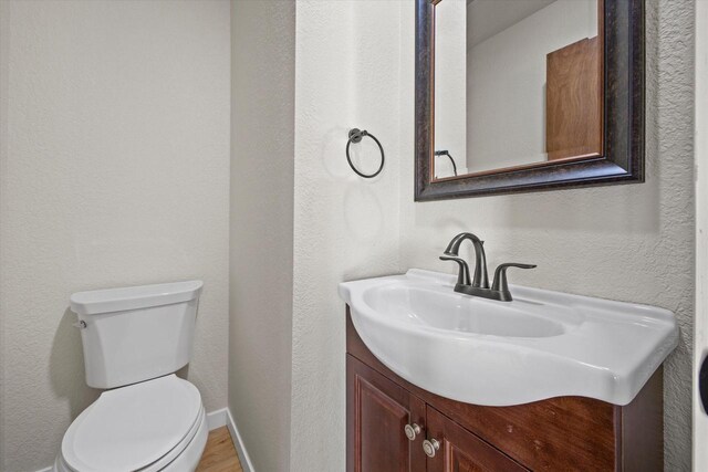 half bathroom with toilet, vanity, and a textured wall