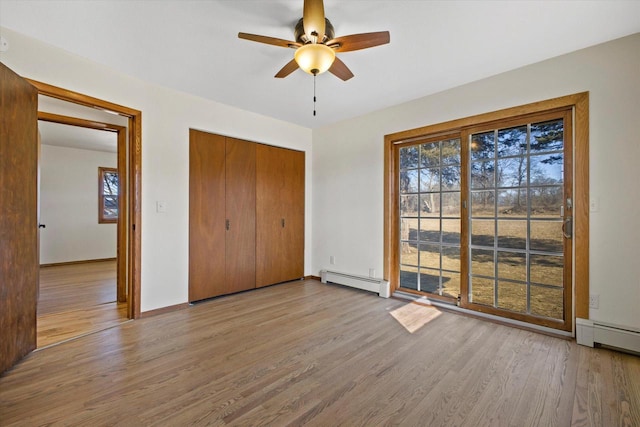 unfurnished bedroom with multiple windows, wood finished floors, a closet, and baseboard heating