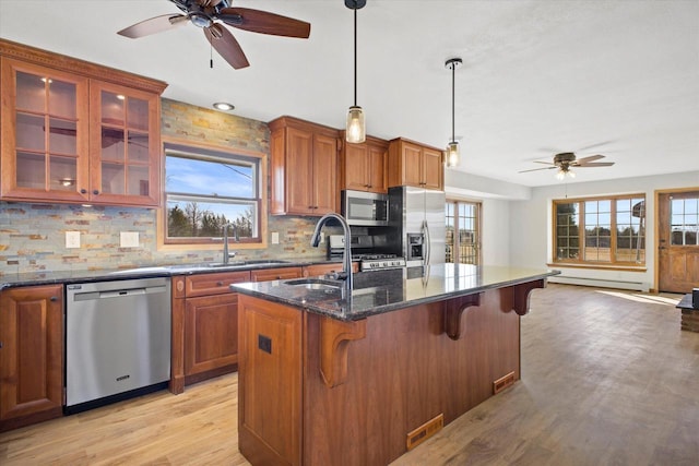 kitchen featuring a breakfast bar, a center island with sink, stainless steel appliances, brown cabinetry, and light wood finished floors