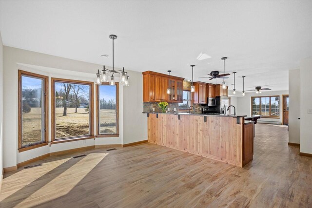 kitchen featuring brown cabinets, a peninsula, light wood-style flooring, open floor plan, and backsplash