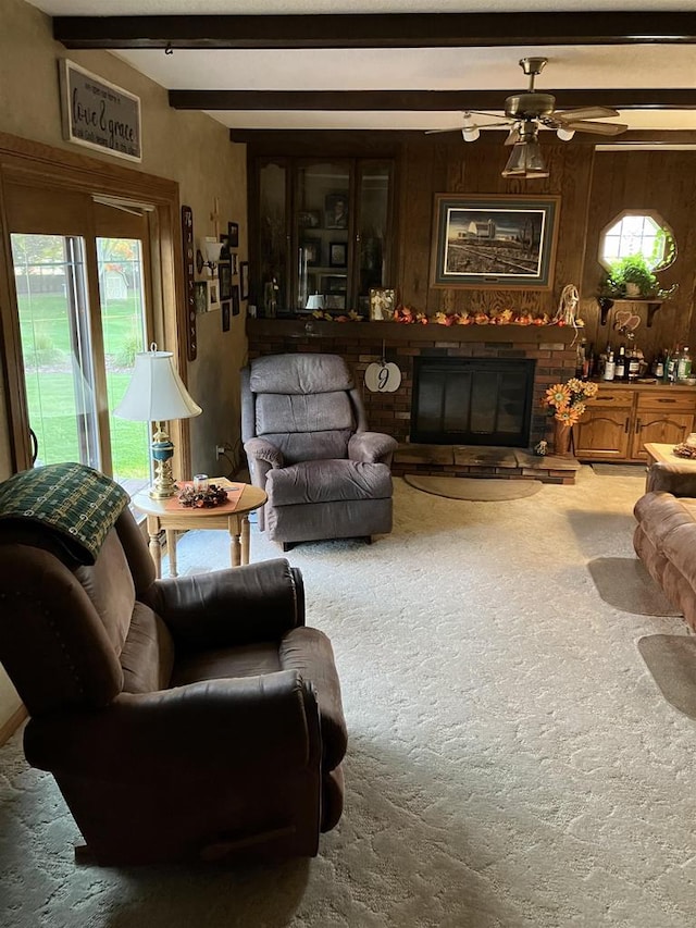 carpeted living room featuring ceiling fan, beamed ceiling, wooden walls, and a glass covered fireplace