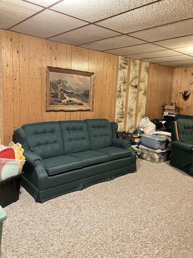 carpeted living area featuring wooden walls and a paneled ceiling