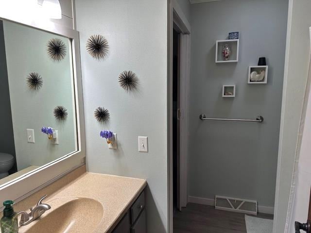 bathroom with visible vents, baseboards, toilet, wood finished floors, and vanity